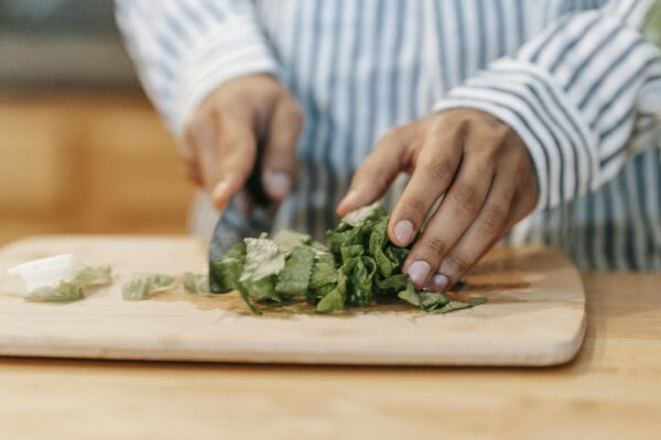Crop man cutting green leaves while preparing healthy food in kitchen