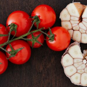 From above of branch of ripe tomatoes and cut garlic on halves placed on wooden table